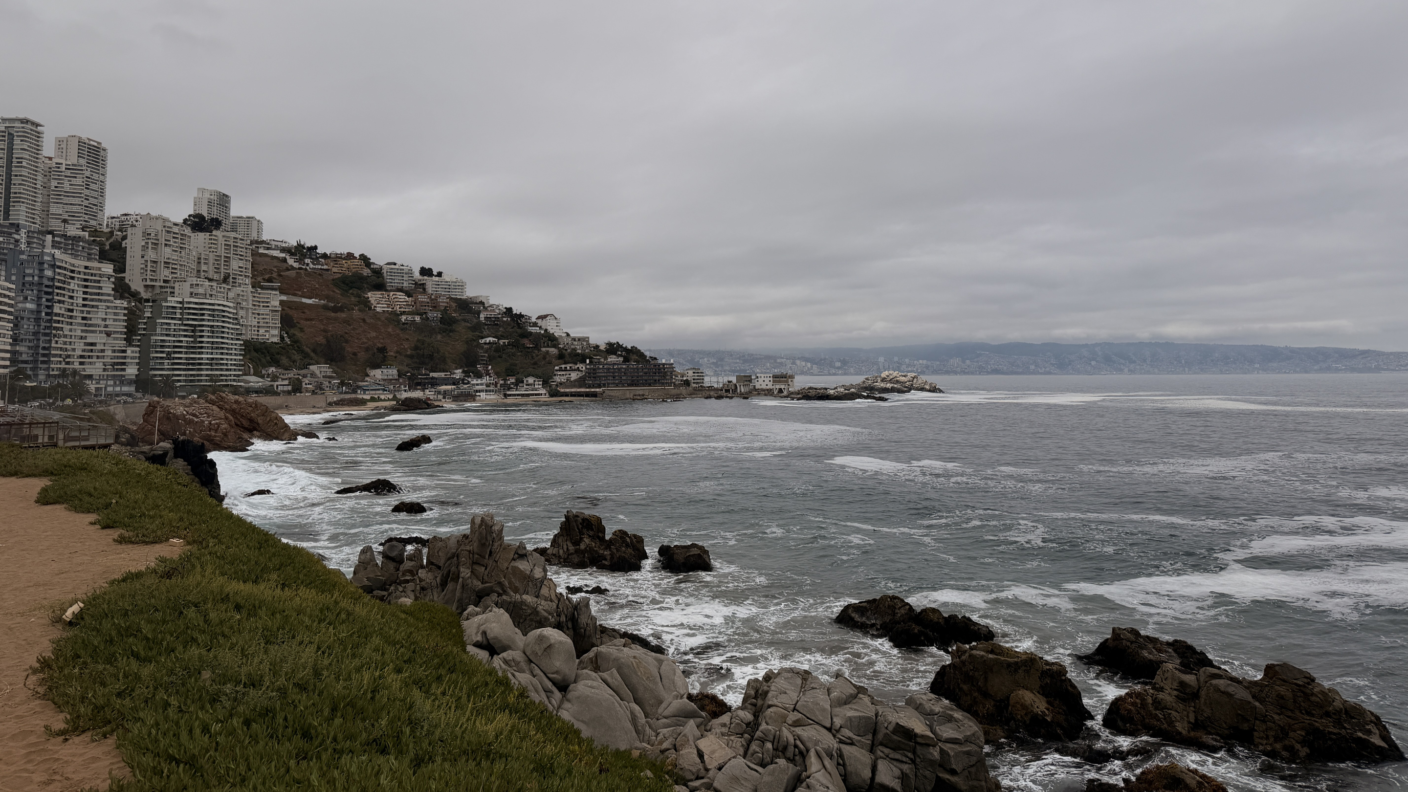 Overcast view of high-rise apartments on a cliff above a rocky Viña del Mar coastline.
