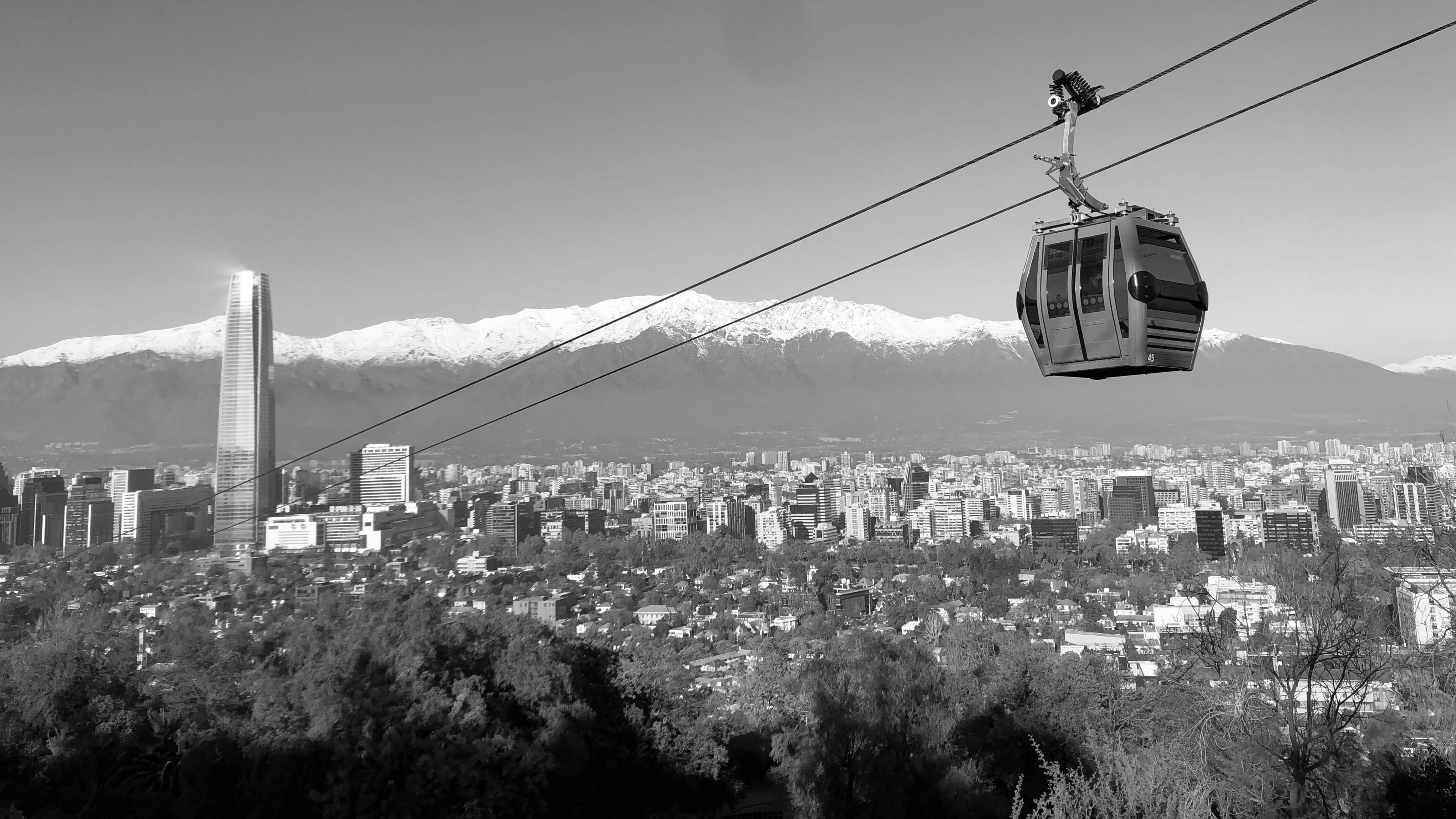 Teleférico sobre Santiago, con la cordillera nevada al fondo, en blanco y negro.
